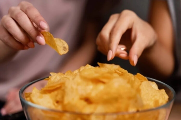 Человек, держащий пустую пачку чипсов, с задумчивым выражением лица, намекающим на неконтролируемое потребление.