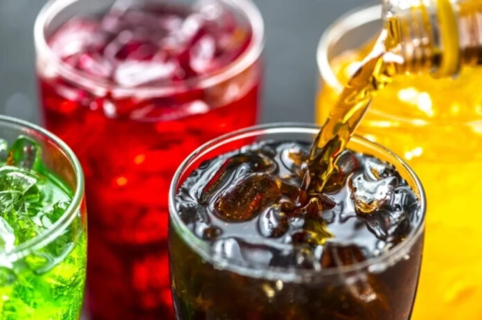 Подросток с задумчивым выражением лица, держащий в руке бутылку газированного напитка, на фоне размытого изображения ночного города.