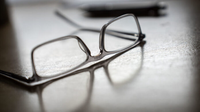 Молодой человек без очков с ясным взглядом, символизирующий отличное зрение, на фоне размытых изображений очков.