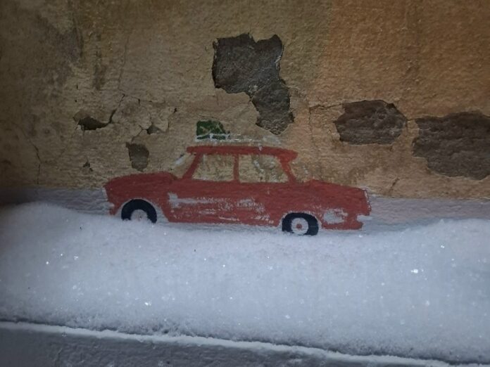 Красная игрушечная машинка, похожая на призрак, стоит на бежевом фоне, символизируя загадочное проникновение игрушечного автопрома в Петербург.