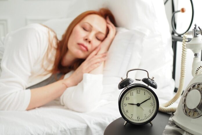 Уставшая сова в пижаме с чашкой кофе, сидящая на стопке книг, символизирующая ночной образ жизни и утренние трудности.