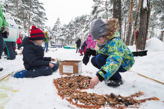 Дети создают кормушку для птиц в виде ресторана на снегу, украшая ее ягодами и семечками