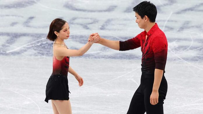 Два фигуриста в ярких костюмах, танцующие на льду в миланском зале, иллюстрирующие необычайное выступление Миуры и Кихары.