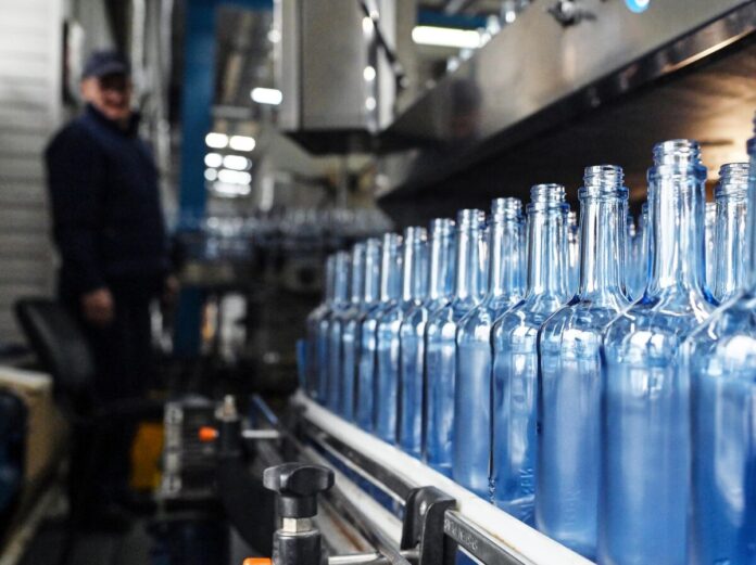 Бутылка водки с этикеткой, изображающей растительные мотивы, на фоне зеленого поля или леса.