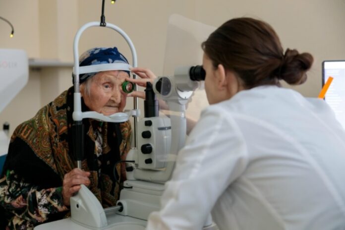 Портрет 111-летней женщины, улыбающейся и смотрящей вдаль, с медицинским персоналом на фоне