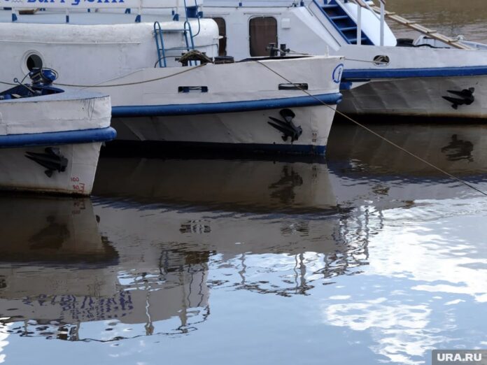 Речной трамвай плывет по реке в Екатеринбурге, на фоне видны городские пейзажи и строящиеся объекты, намекающие на развитие водного транспорта.